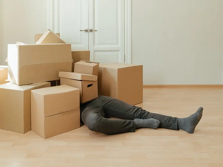 a person laying on a wooden floor under a pile of cardboard boxes representing a slip and fall accident claim